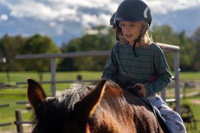 Kind mit Reithelm sitzt auf Pferd während Reitunterricht auf dem Platz