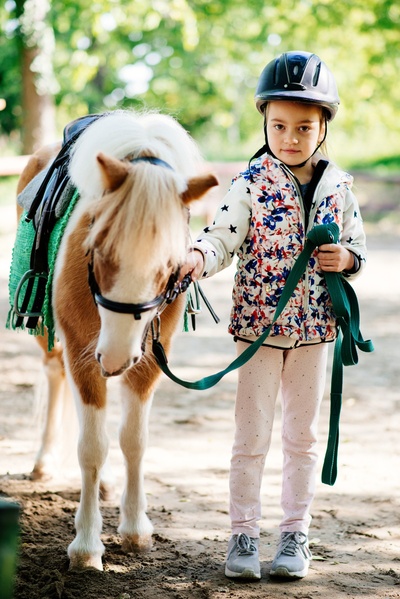 Kleines Mädchen mit Pony an der Hand im Reitstall