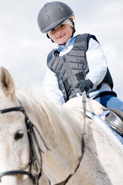 Junge beim Reiten auf einem weißen Pferd mit Sicherheitsweste und Reithelm