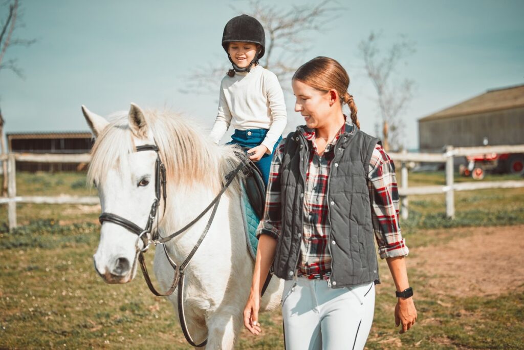 Mädchen auf weißem Pferd wird von Reitlehrerin geführt