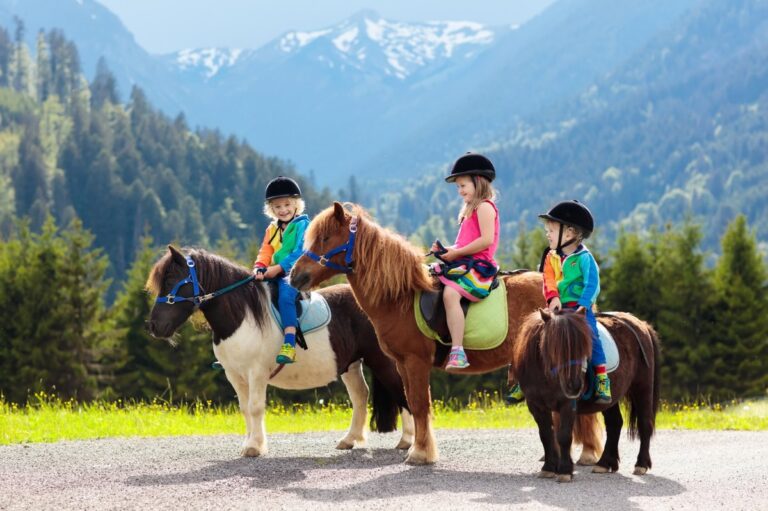 Kinder reiten auf kleinen Ponys in bunter Kleidung vor beeindruckender Bergkulisse