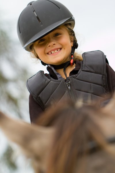 Mädchen mit Reithelm auf einem Pferd lächelt in die Kamera