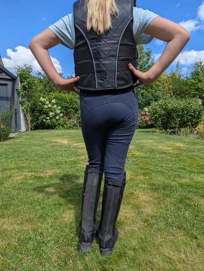 Kind mit schwarzer Schutzweste von hinten in Reitkleidung